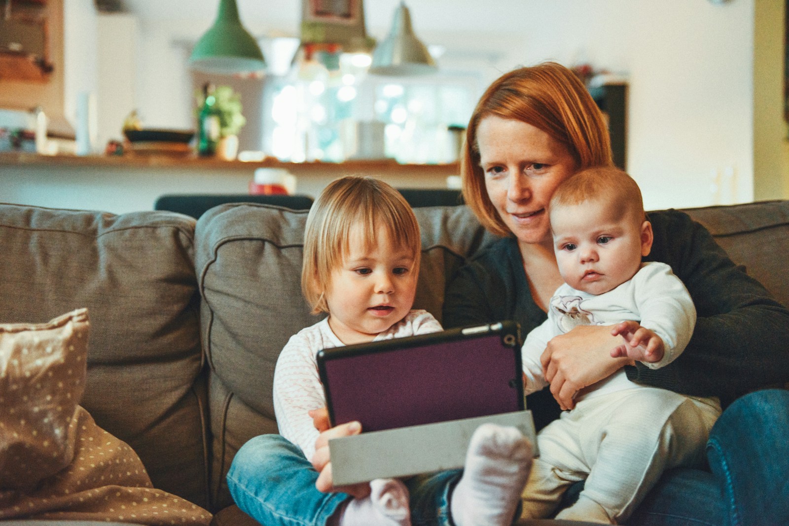 two babies and woman with homeowners insurance sitting on sofa while holding baby and watching on tablet